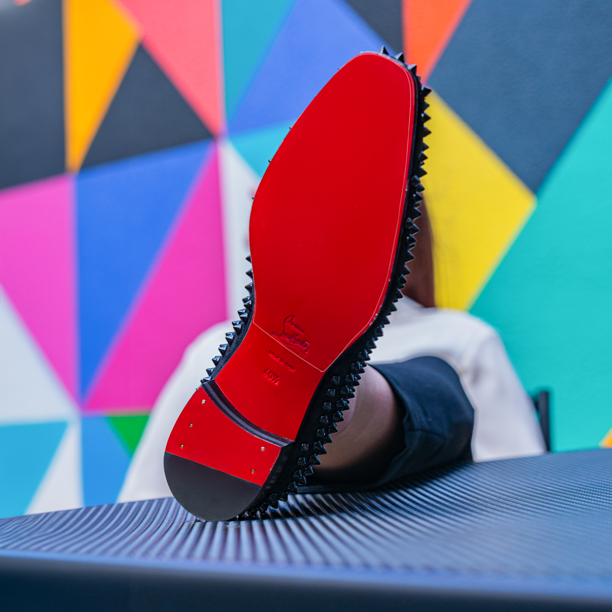 Christian Louboutin Loafers Sole Guard featuring a red sole and spikes are showcased against a colorful geometric background.