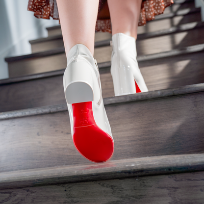 As they walk upstairs, the chic Christian Louboutin Turelastic Boots reveal vibrant red soles under their white high heels. A swaying brown polka dot skirt complements the look, while Sole Guards protect these durable vinyl polymer masterpieces.