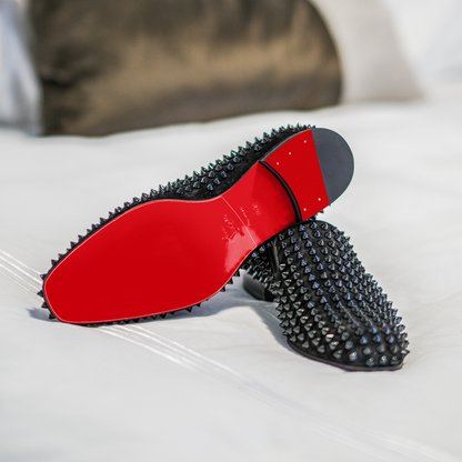 Christian Louboutin Loafers Sole Guard featuring black studs and glossy red soles, elegantly displayed on a white bedspread.