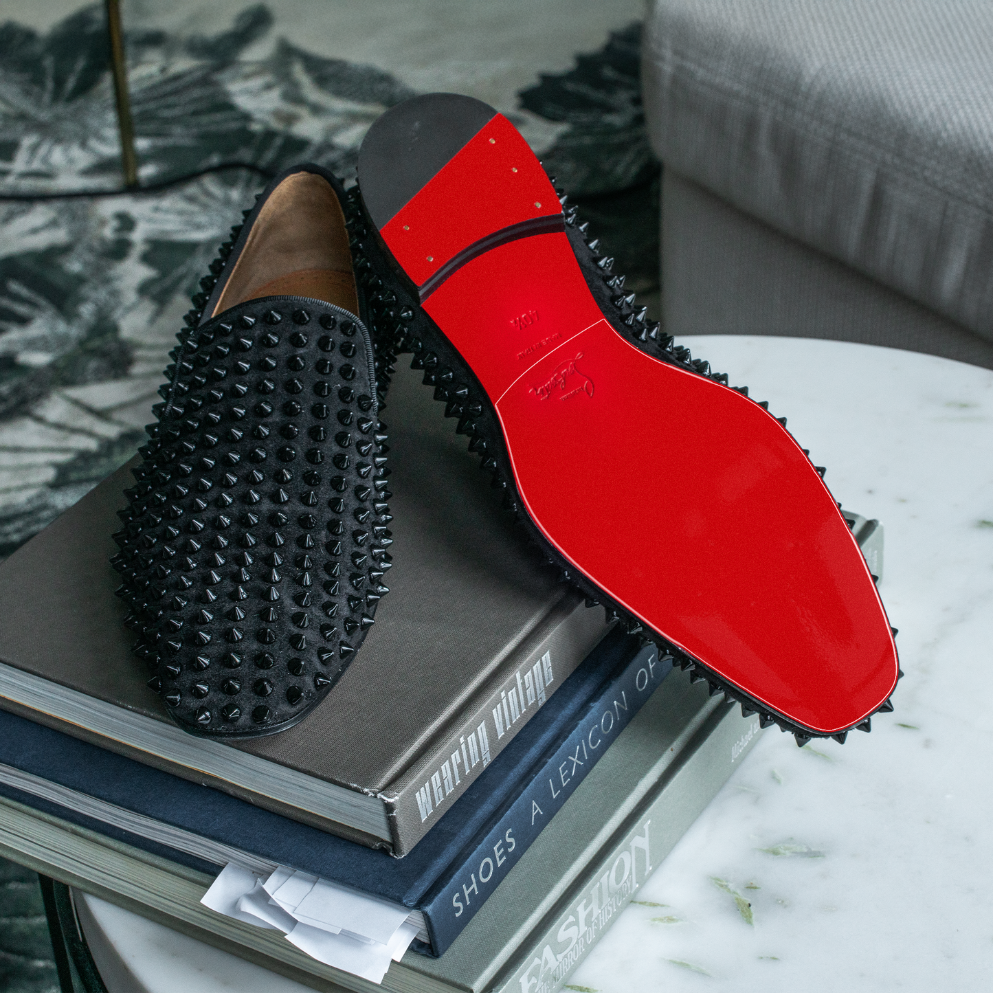 Christian Louboutin loafers with red soles rest elegantly on stacked fashion books, safeguarded by the Sole Guard 3 Pack to maintain their pristine condition.