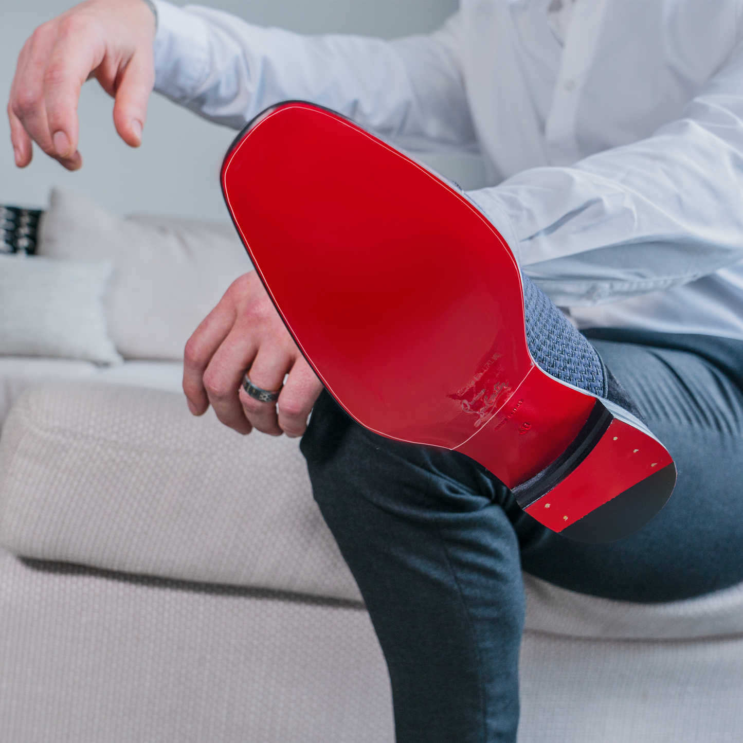 A person sits on the couch, proudly displaying their shiny Christian Louboutin red-soled shoe, protected by a Christian Louboutin Oxfords Sole Guard, maintaining its pristine allure.