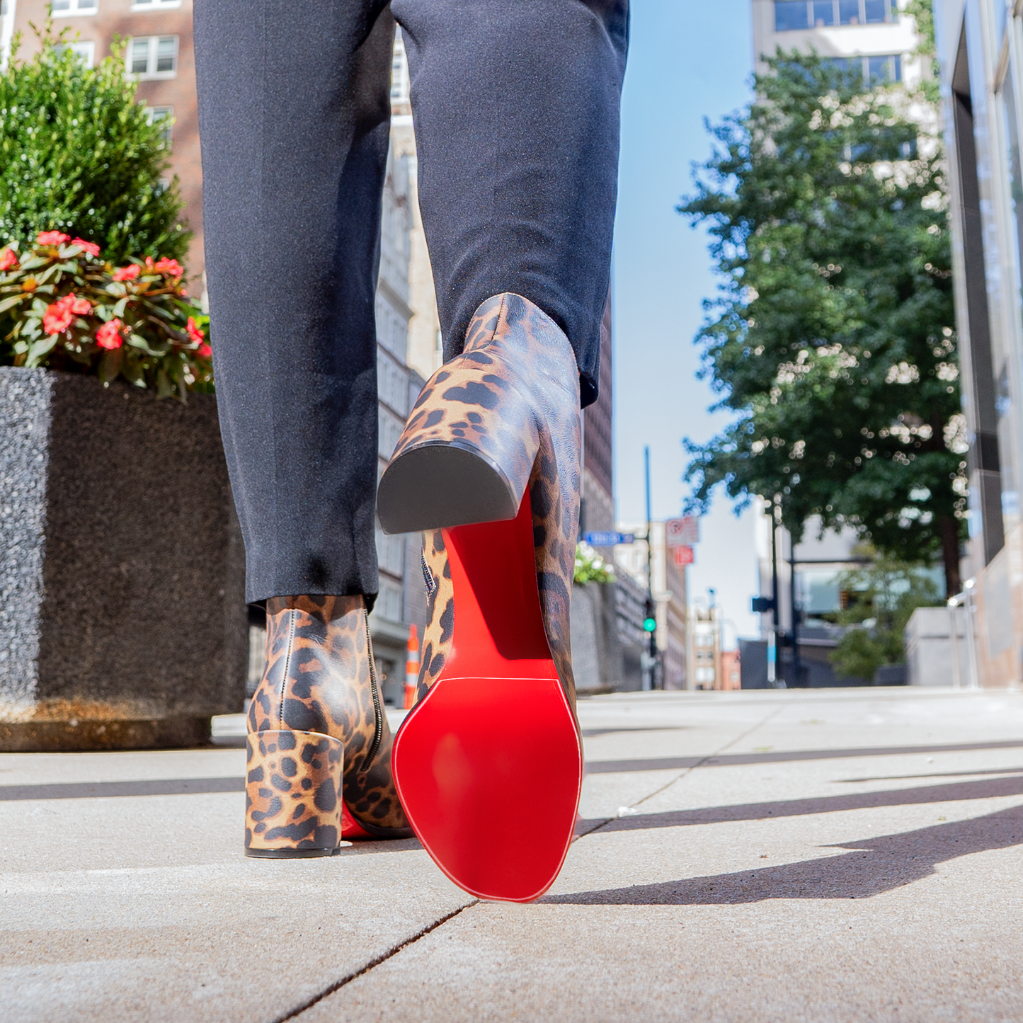 A person strolls through the city in eye-catching Christian Louboutin Block Heel Boots with iconic red soles and leopard print, complemented by sleek black pants. These chic boots also feature a Sole Guard for designer shoe protection.